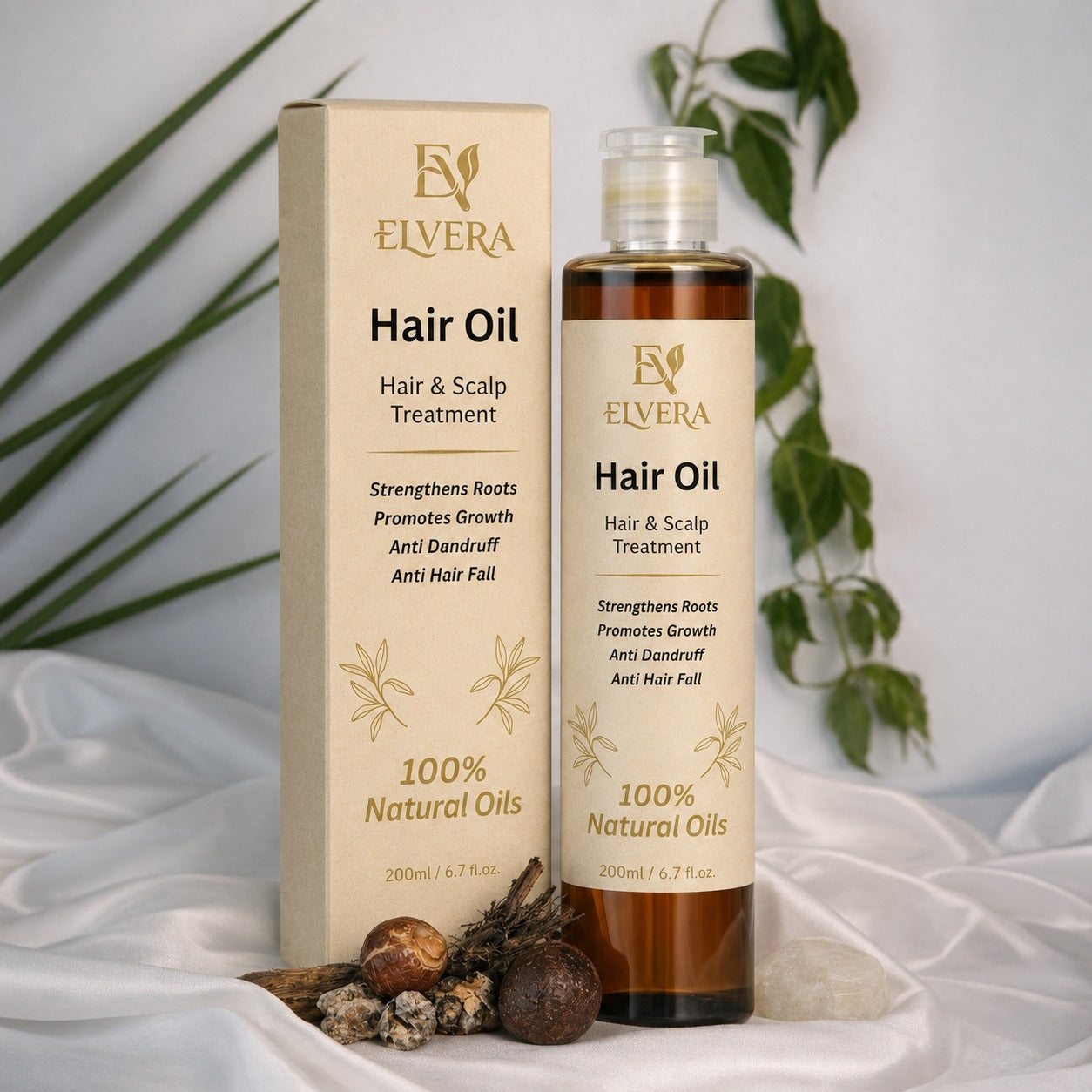 Elvera Hair Oil bottle and packaging on a white fabric background with green leaves.
